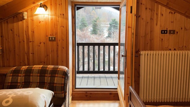 Una habitación de cabaña de madera con una cama, una ventana y una puerta que da a un balcón.