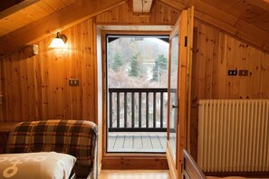 A wooden cabin room with a bed, a window, and a door leading to a balcony.