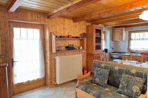 A wooden interior with a sofa, a radiator, a kitchen area, and a window.