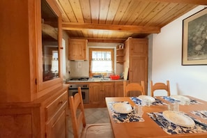 A wooden kitchen with a dining table set for four, a window with a view, and wooden cabinets.