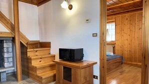Una escalera de madera lleva a un dormitorio con una cama y una pequeña mesa de madera con un microondas.