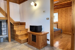 A wooden staircase leading to a bedroom with a bed and a small wooden table with a microwave.