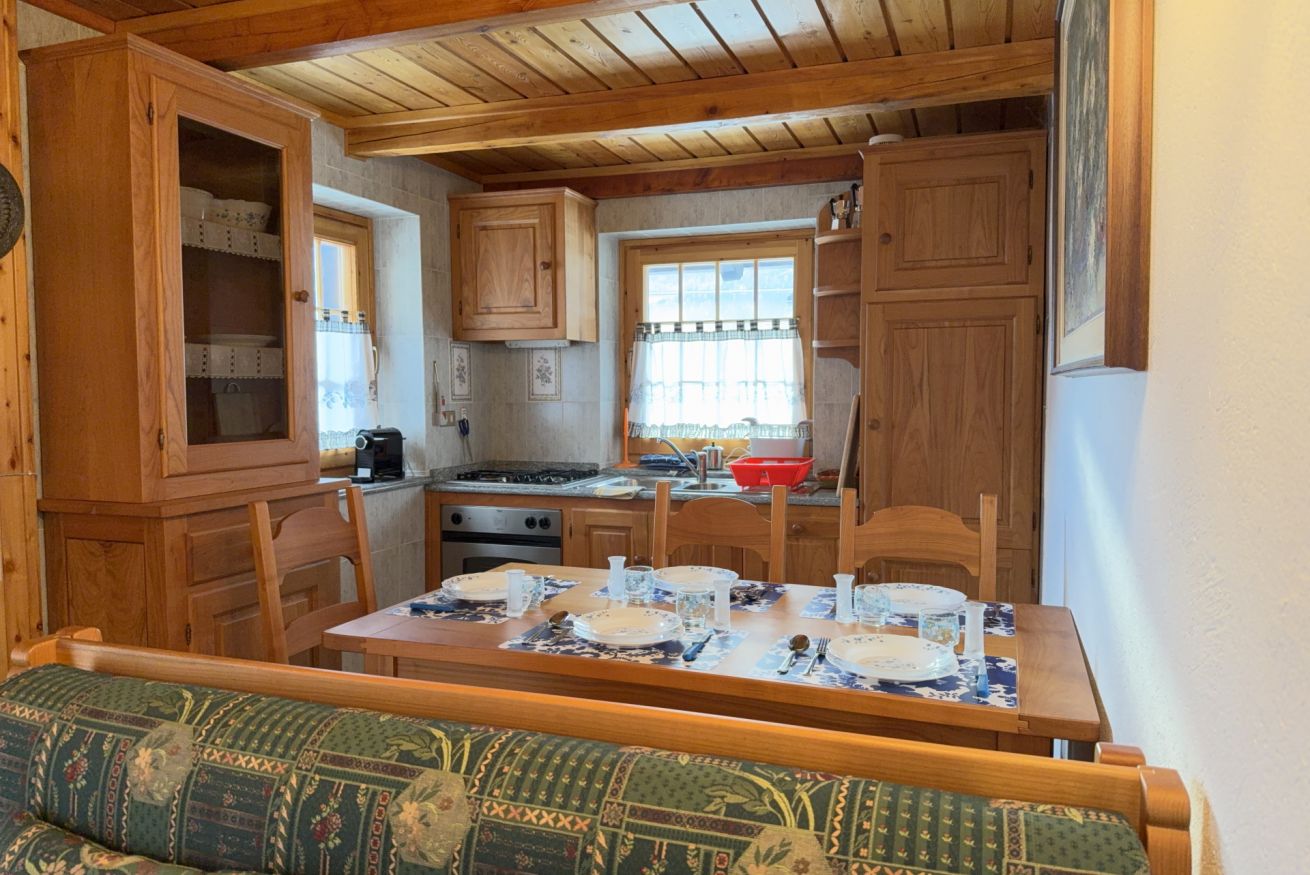 A compact kitchen with wooden cabinets, a dining table set for four, and a bench with patterned upholstery.