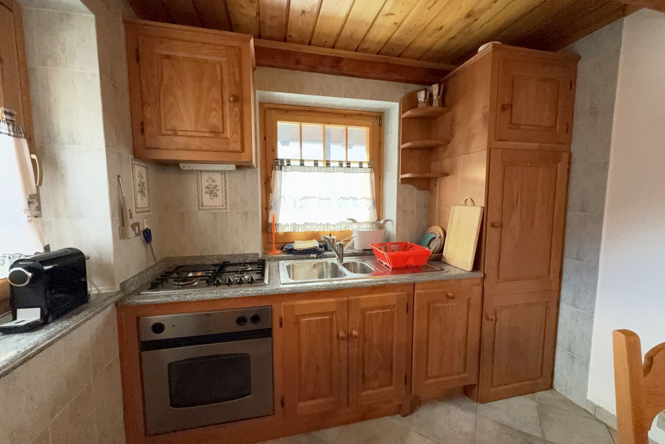 Una cocina con armarios de madera, estufa a gas, lavabo y una ventana con cortinas.