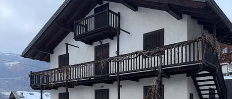 A two-story building with balconies, a sloped roof, and a mountainous backdrop.