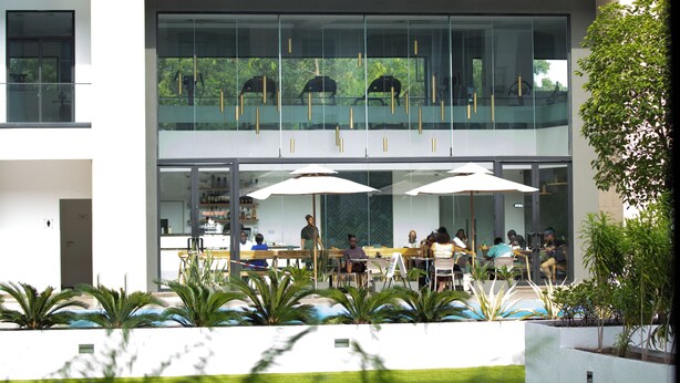 A modern outdoor dining area with glass walls, umbrellas, and seating. - VIP at Embassy Gardens  (Accra)