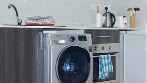 A compact kitchen with a built-in washer and dryer, a stainless steel oven, and a microwave. - VIP at Embassy Gardens  (Accra)