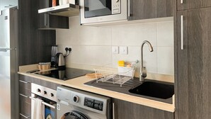 A compact kitchen with a built-in microwave, a stainless steel sink, a kettle, and a washing machine. - VIP at Embassy Gardens  (Accra)