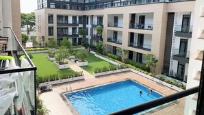 A modern building with multiple balconies, a central courtyard with greenery, and a swimming pool. - VIP at Embassy Gardens  (Accra)