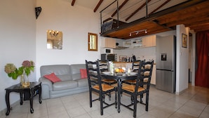 A living room with a grey sofa, a dining table with chairs, a kitchen area with a refrigerator, and a staircase. - Cozy apartment in Cuttoli with WiFi (Cuttoli)