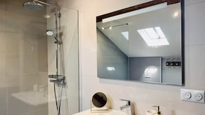 Ein modernes Badezimmer mit einer Duschkabine aus Glas, einem großen Spiegel und einem weißen Waschbecken.