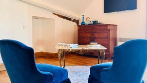 Ein Zimmer mit zwei blauen Stühlen, einem Holzschrank, einem Tisch mit weißer Tischdecke und einem Flachbildfernseher an der Wand.