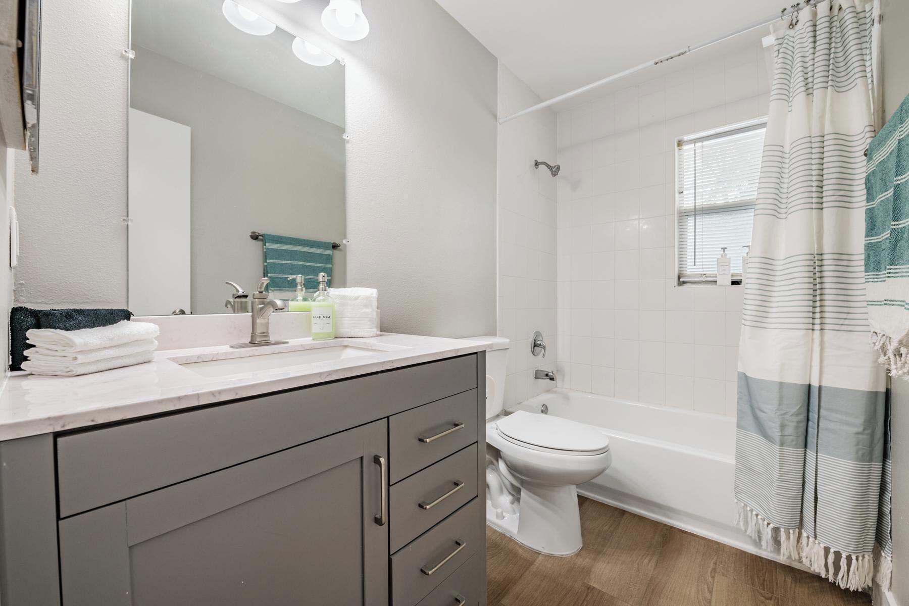 A modern bathroom with a vanity, sink, mirror, and a shower with a striped curtain.