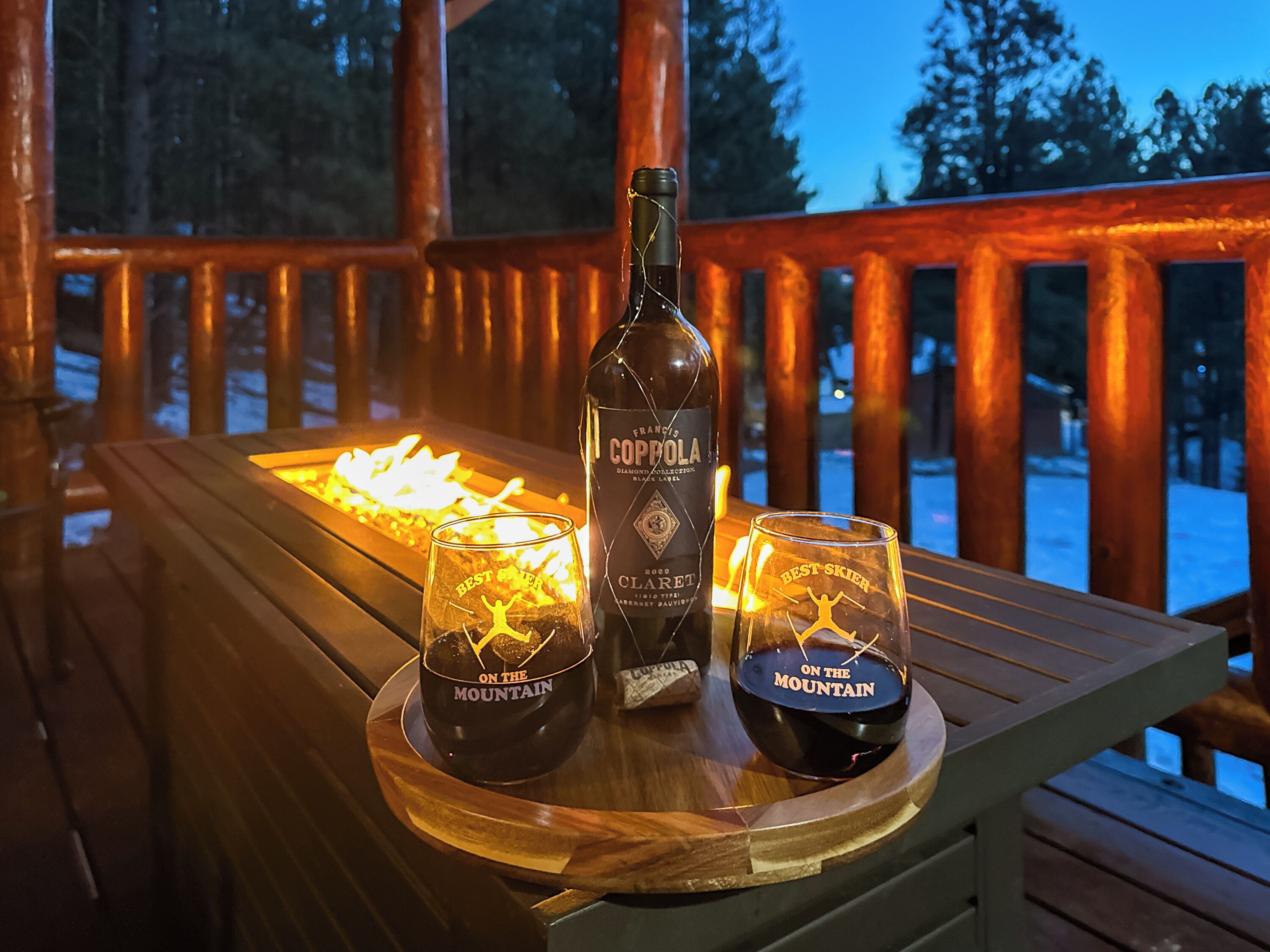 Een fles Coppola-wijn en twee glazen op een houten tafel, met een haardvuur op de achtergrond.
