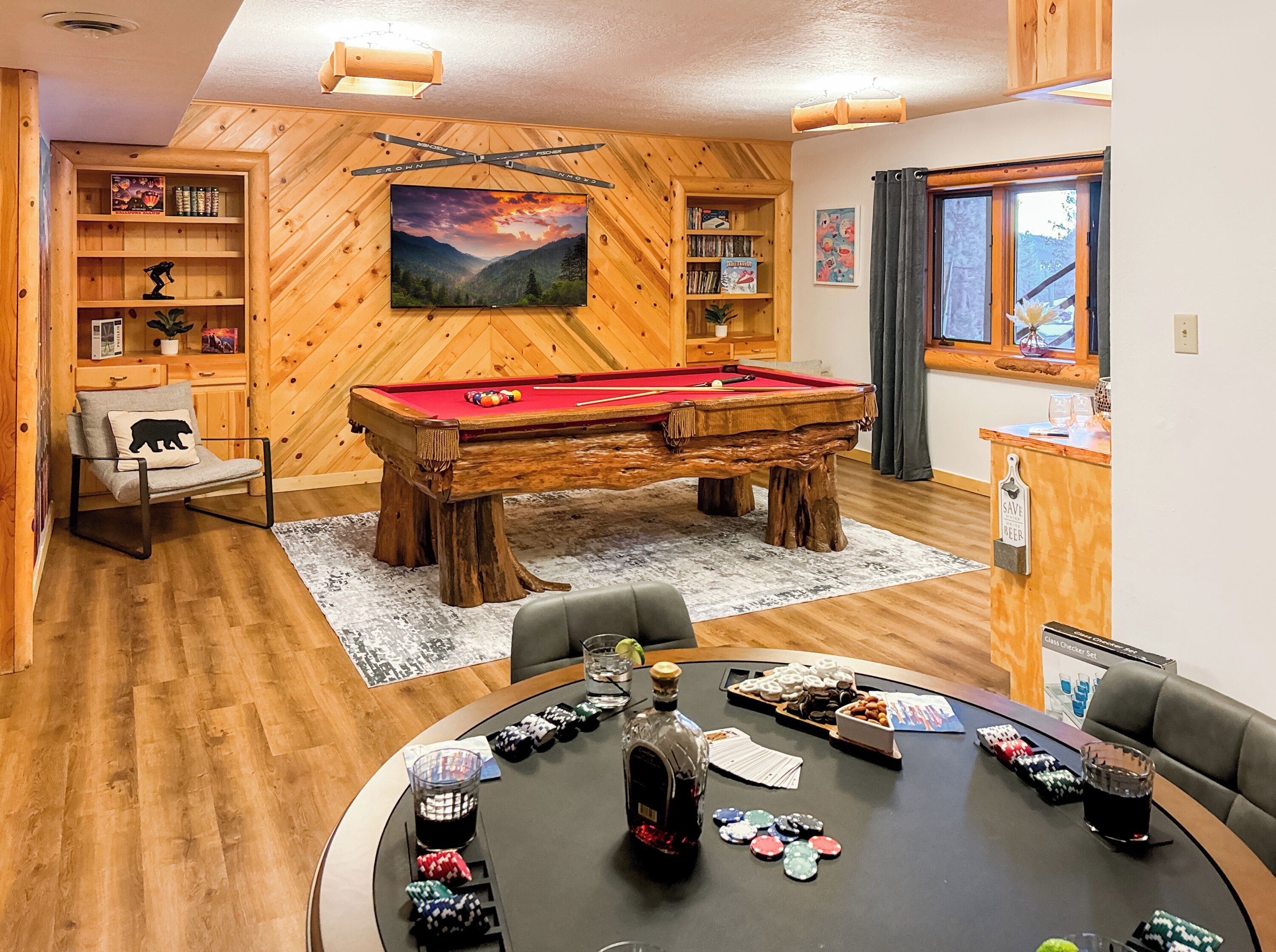 A cozy room with a pool table, a poker table, wooden bookshelves, and a large painting.