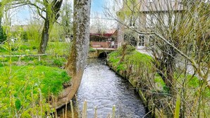 A narrow water channel with a bridge, surrounded by greenery and a building in the background. - Beautiful home in Renty with WiFi (Renty)