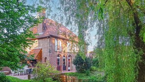 A traditional brick house with a tiled roof, surrounded by lush greenery and a small stream. - Beautiful home in Renty with WiFi (Renty)