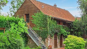A rustic wooden building with a sloped red-tiled roof, a wooden staircase leading to the entrance, and a brick wall with a wooden door. - 1 bedroom cozy home in RENTY (RENTY)