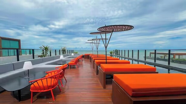 Eine Dachterrasse mit orangefarbenen Sitzgelegenheiten, einem Holzboden und Blick auf das Meer.