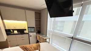 Ein Hotelzimmer mit einem Bett, einem an der Wand befestigten Fernseher, einer Küchenzeile und einem großen Fenster.