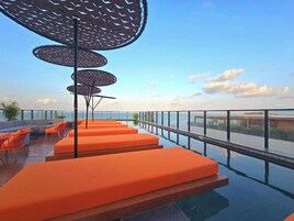 Terraço no telhado com assentos laranja e guarda-corpo de vidro, com vista para o mar.