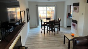 A modern living room with a flat-screen TV, dining area with a wooden table and chairs, a small table with a candle, and a brown leather sofa. - Delightful 2-bedroom house in Incline Village near the lake (Incline Village)