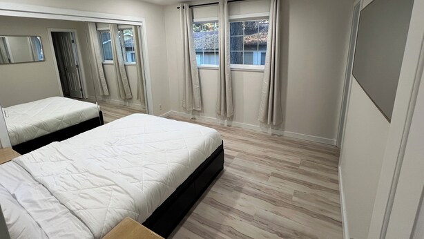 A bedroom with two beds, a large window with curtains, a mirror, and a door. - Delightful 2-bedroom house in Incline Village near the lake (Incline Village)
