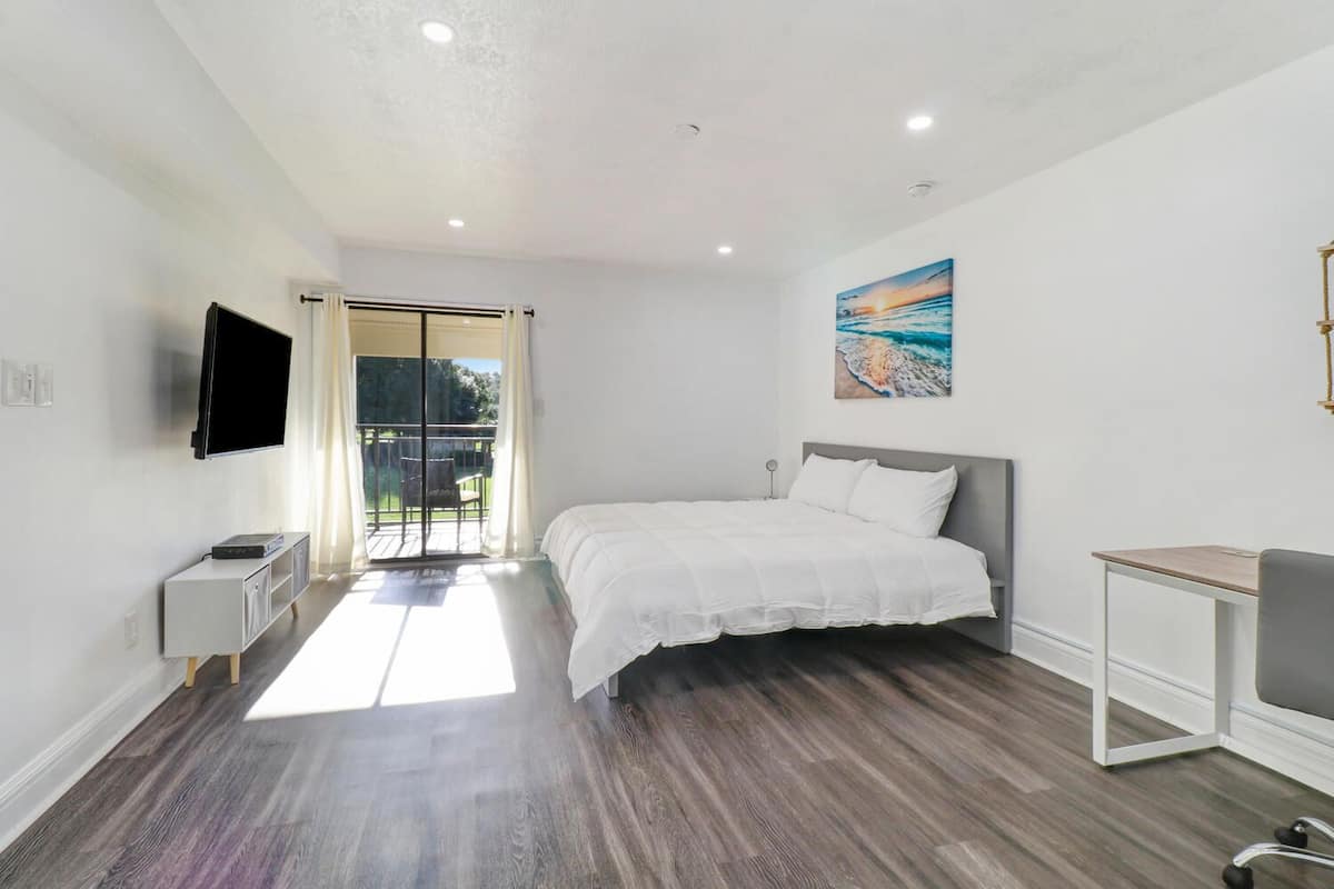 A bedroom with a bed, a TV, a desk, and a balcony.
