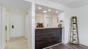 A modern kitchen with dark wood accents, a built-in island, and a wooden ladder shelf with plants. - Saddlebrook Golf Course Condo Voila Rent (Wesley Chapel)