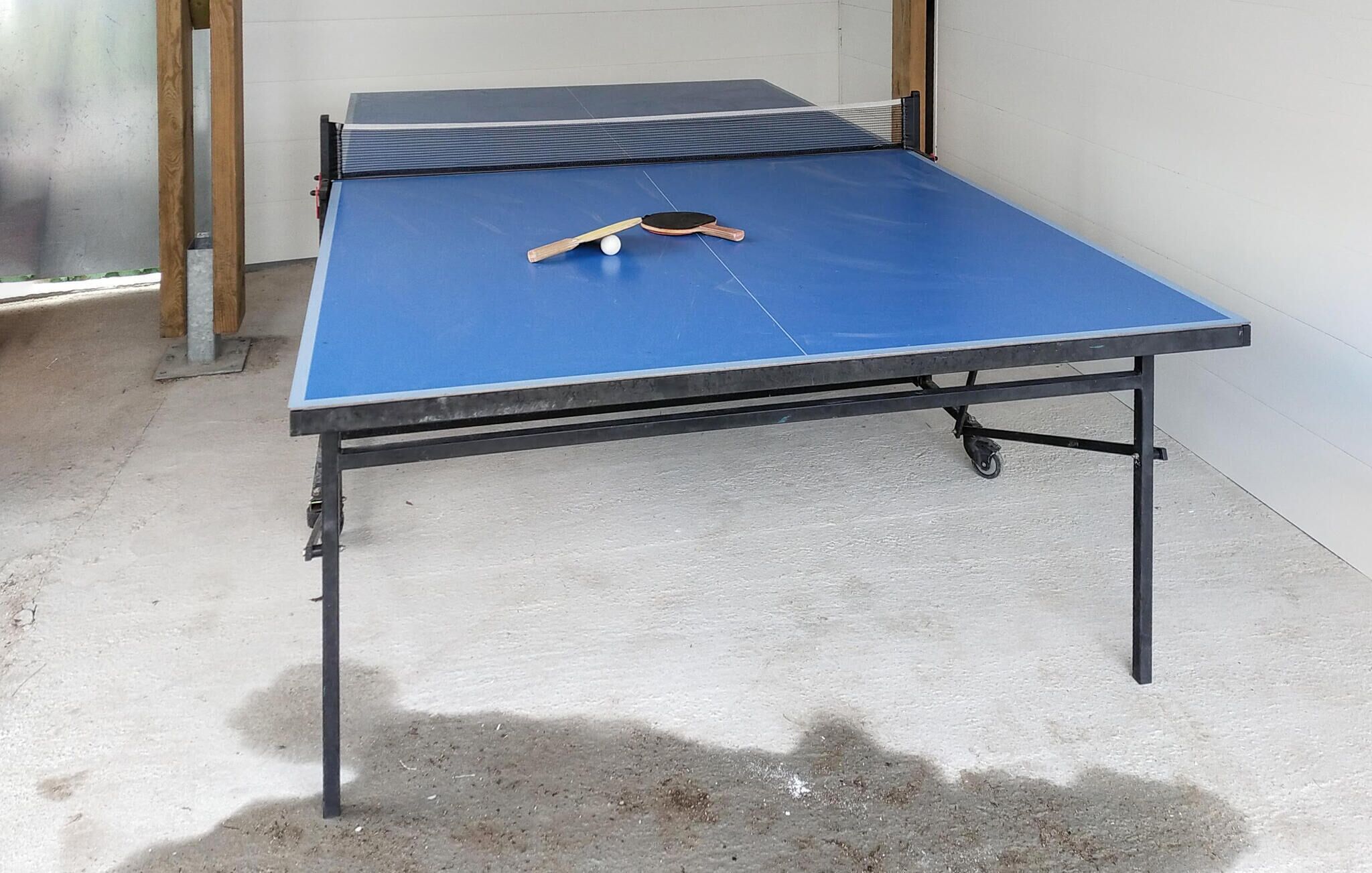 A ping pong table with a blue playing surface, a paddle, and a ball.