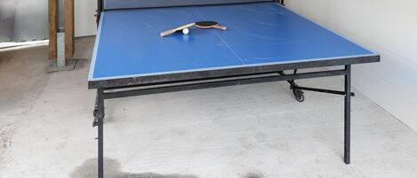 A ping pong table with a blue playing surface, a paddle, and a ball.