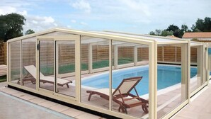 A covered swimming pool with a glass enclosure, wooden deck, and lounge chairs. - Stunning home in La Barre de Monts (La Barre de Monts)