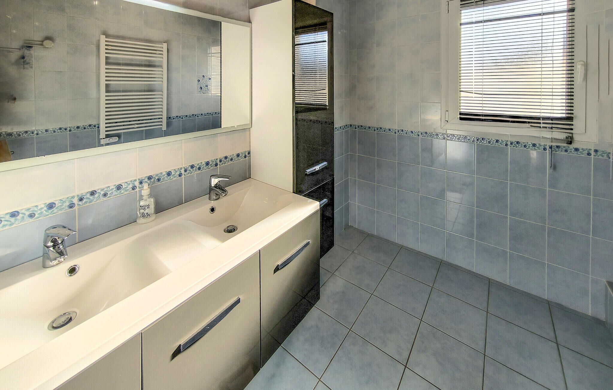 A bathroom with a white sink, two faucets, a mirror, and a window with blinds.