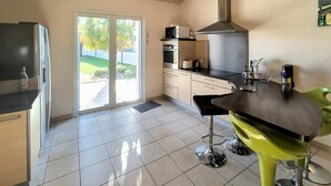 A modern kitchen with a sliding glass door leading to a patio, a stainless steel range hood, and a bar area with stools. - Stunning home in La Barre de Monts (La Barre de Monts)