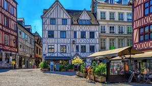 A cobblestone street with traditional half-timbered buildings, a café with outdoor seating, and a bicycle parked nearby. - Urszula, charmant studio proche du Vieux Marché (Rouen)