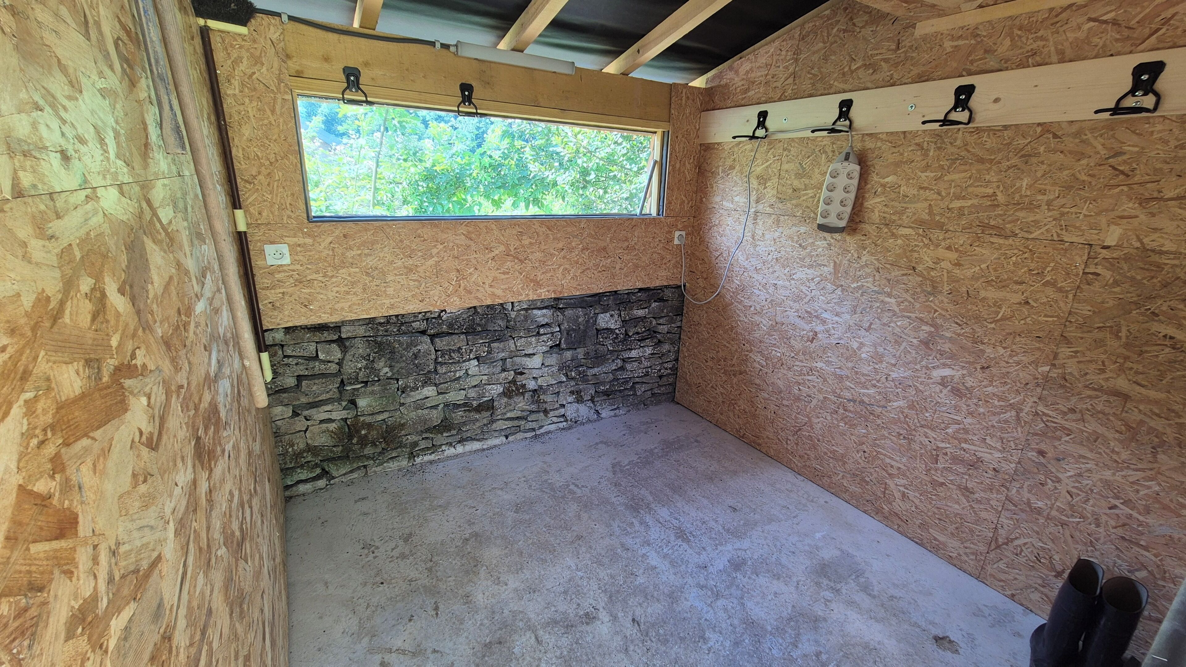A room with a stone wall, a window, and a power outlet on the wall.