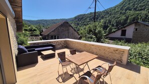 Une terrasse dotée de meubles en osier, d’un mur en pierre et offrant une vue sur une colline boisée.