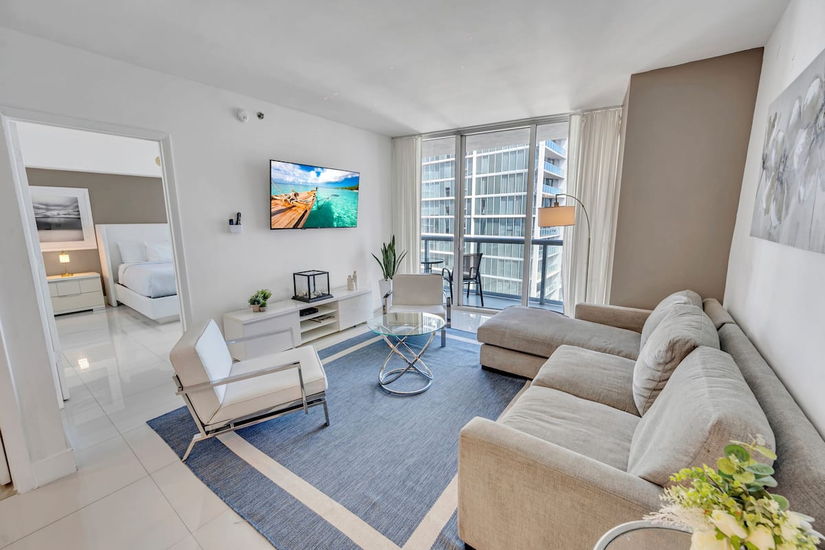 A modern living room with a sofa, a glass coffee table, and a TV mounted on the wall.