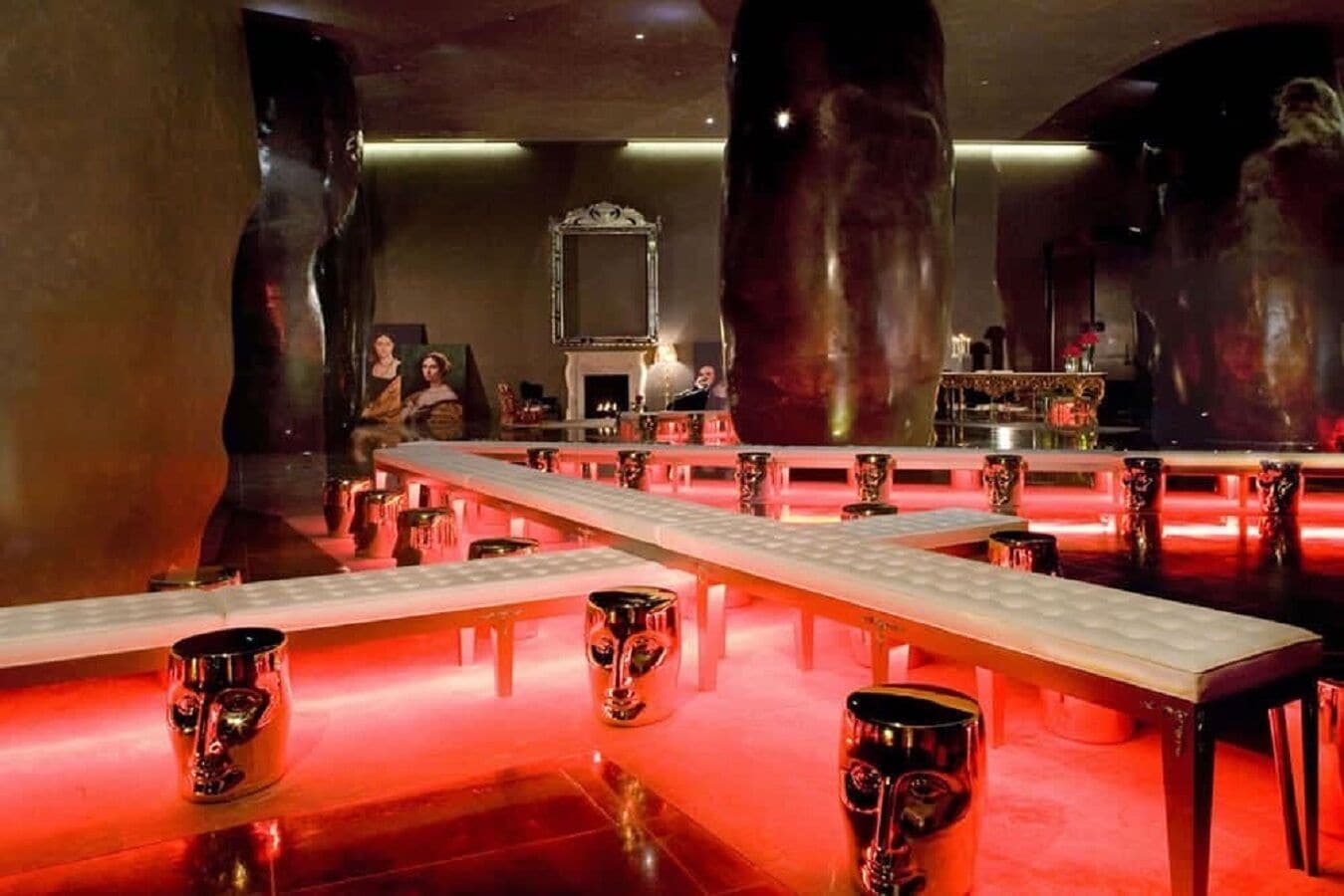 Una zona de bar con mesas largas, taburetes y un espejo.
