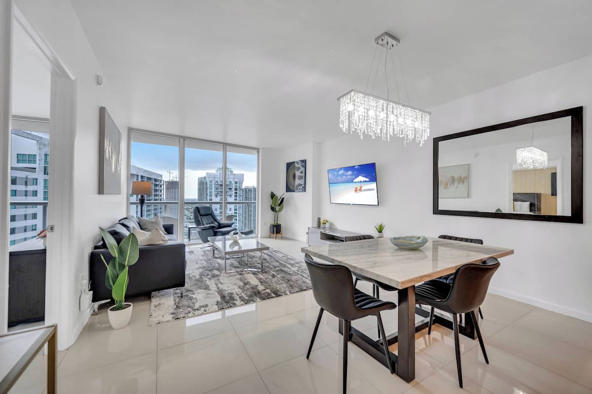 A modern living room with a large window, a dining area with a marble table, and a city view.
