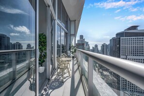 A balcony with a glass railing, a potted plant, and a table with chairs.
