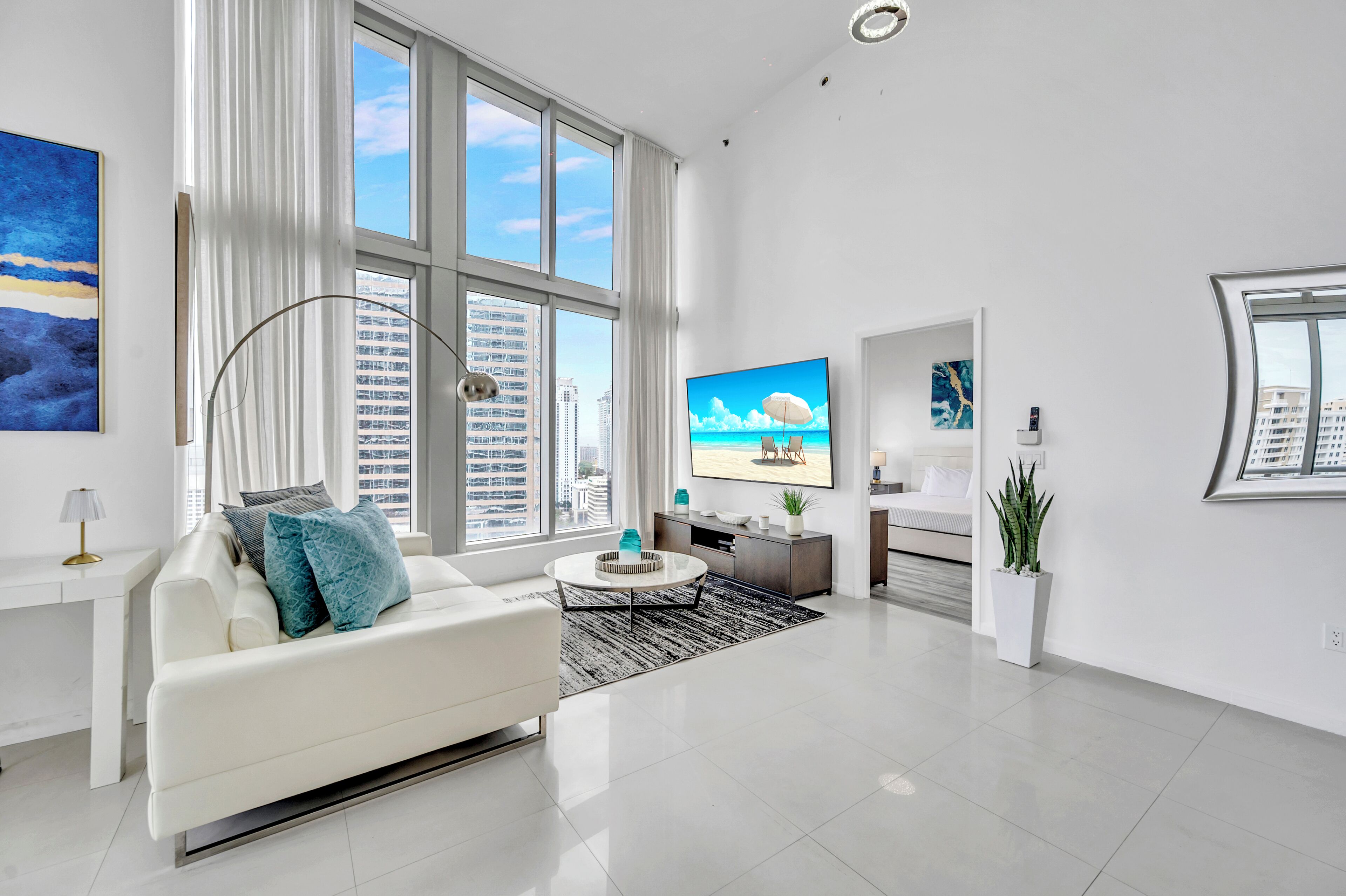 A modern living room with a white sofa, a coffee table, and a TV displaying a beach scene.