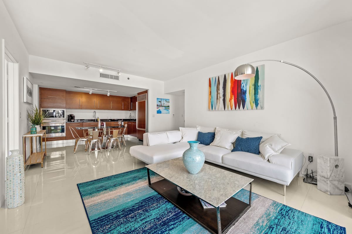 A modern living room with a white sofa, a coffee table, and a colorful rug.