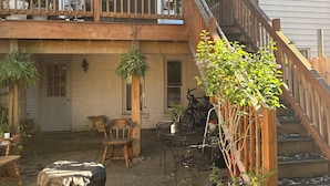 A residential backyard with a wooden deck, potted plants, outdoor furniture, and a staircase leading to a second floor.