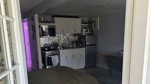 A compact living space with a kitchenette, a bed, and a wicker chair.