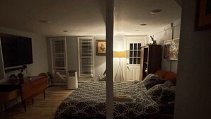 A dimly lit bedroom with a bed, a desk, a chair, and a television.