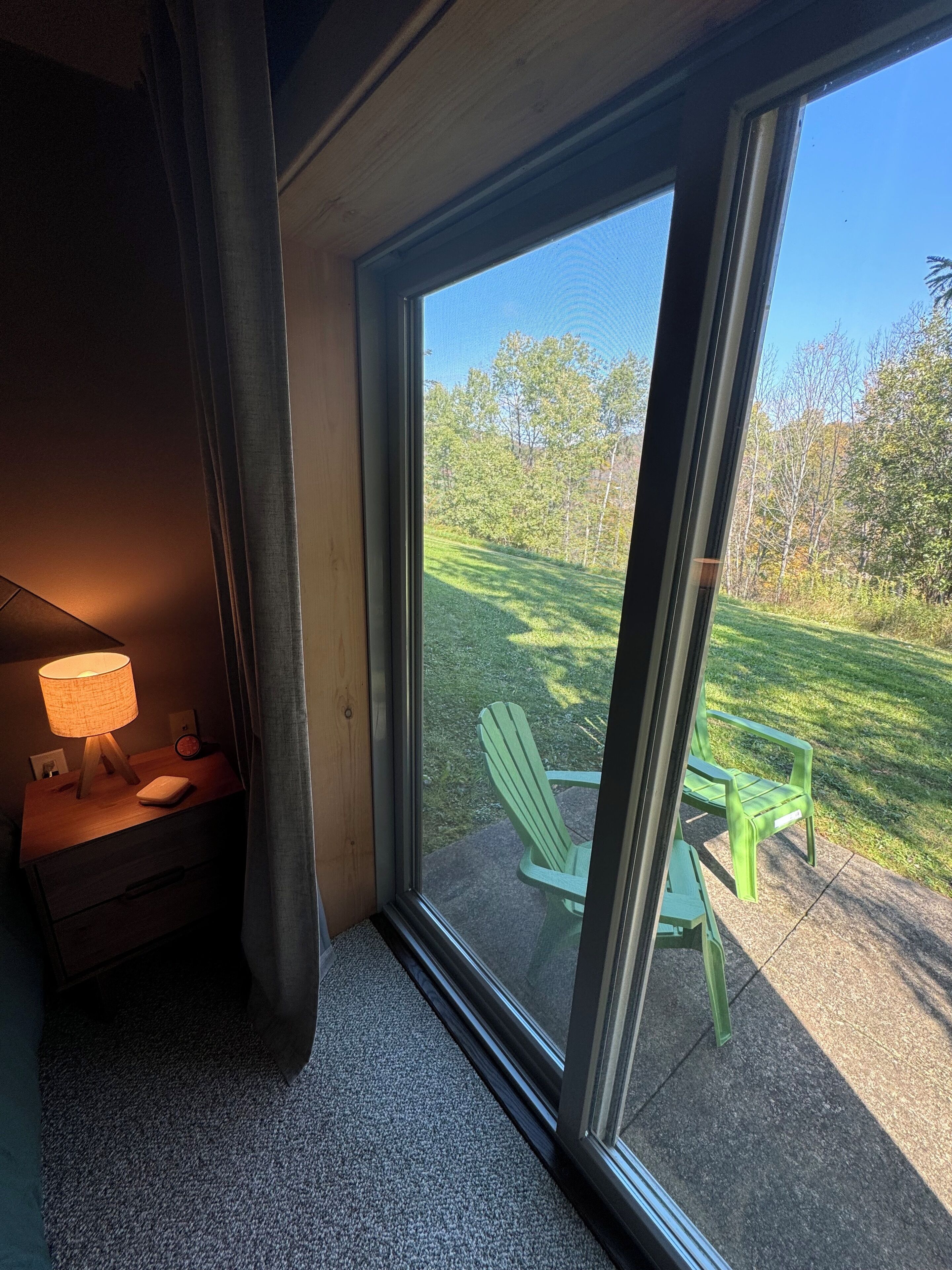 A room with a large window, a green chair, and a table outside.