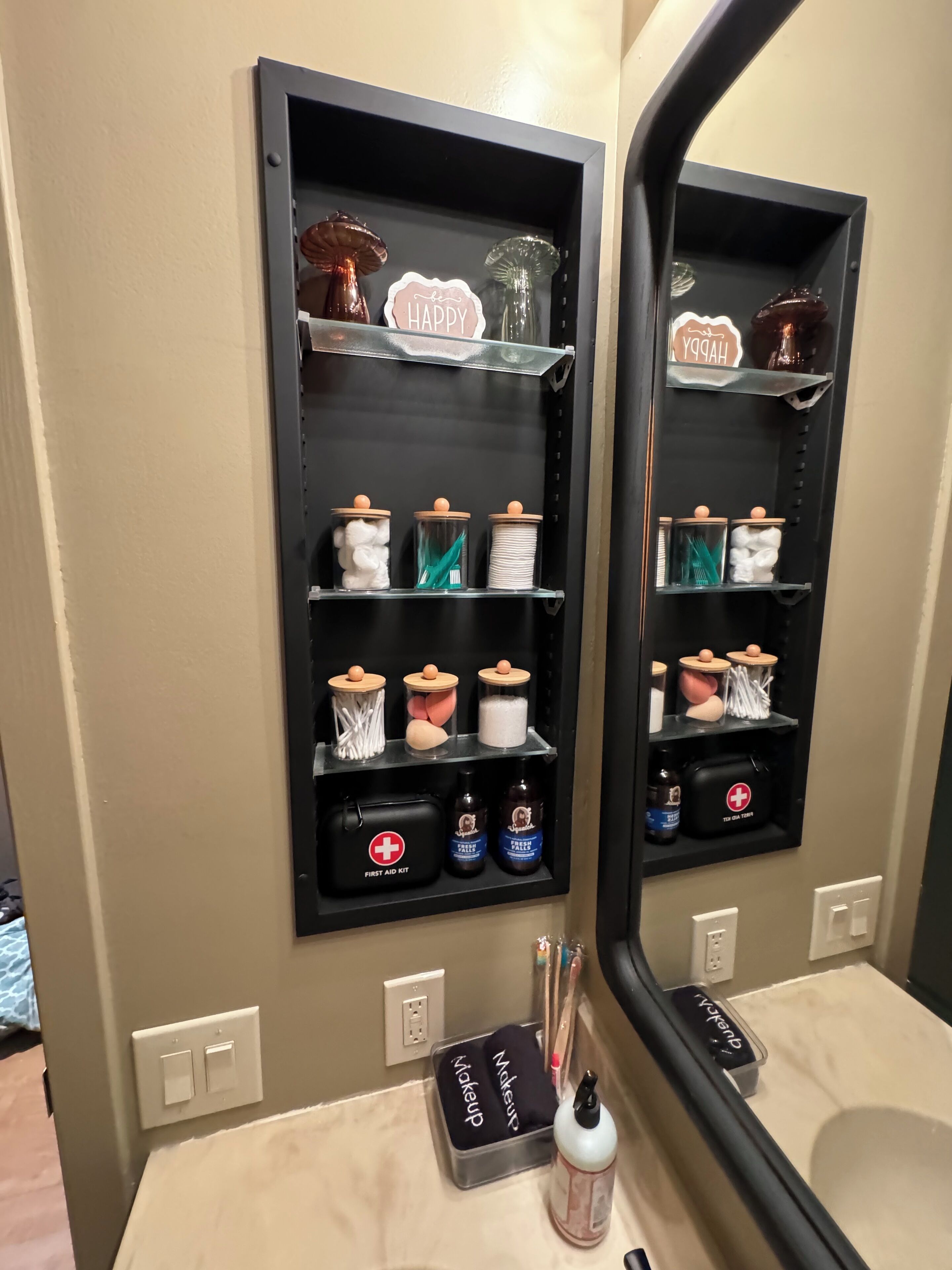 A bathroom with a black shelf unit containing toiletries, a first aid kit, and a makeup bag.