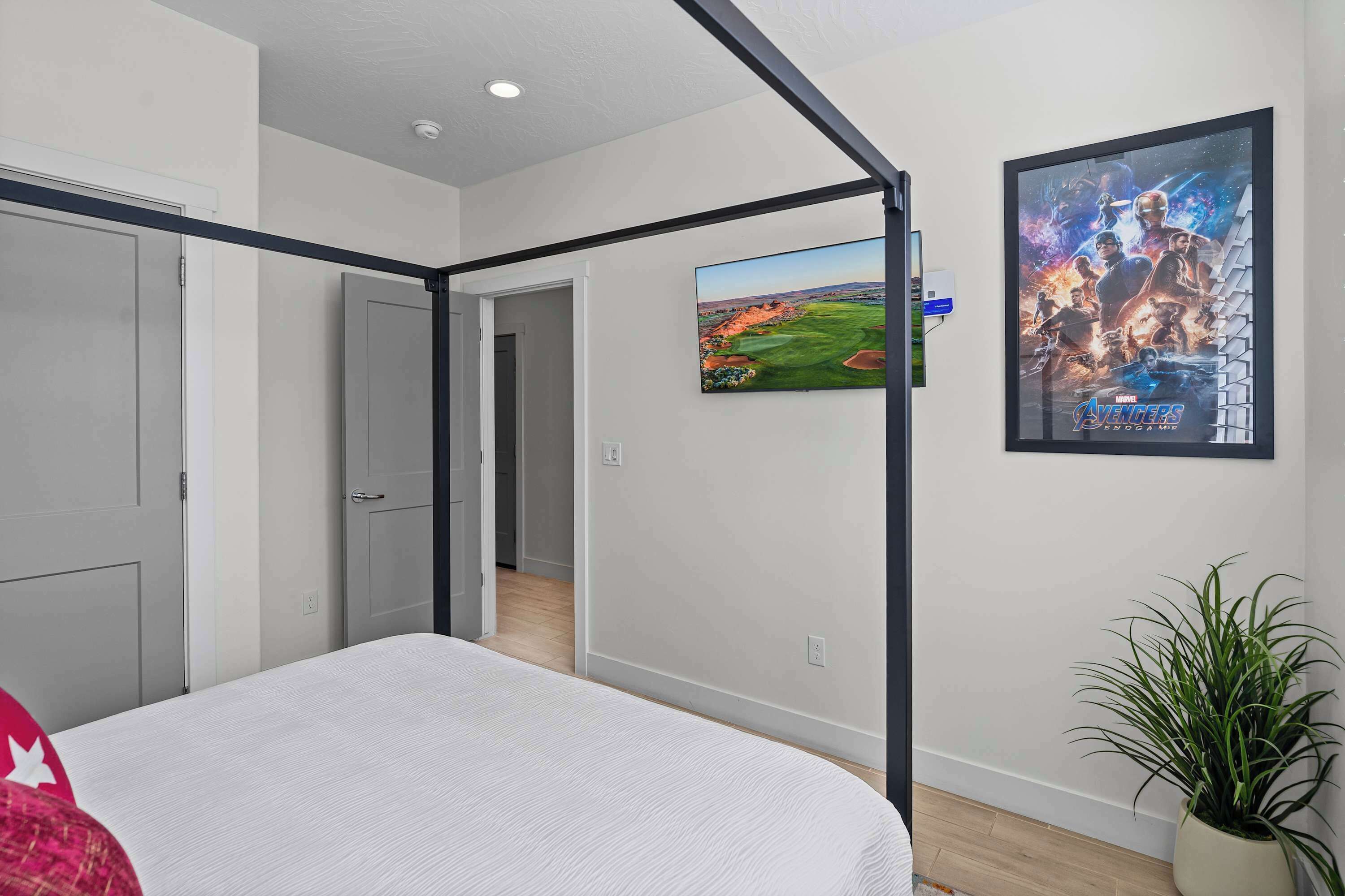 A bedroom with a four-poster bed, a large poster on the wall, and a potted plant.