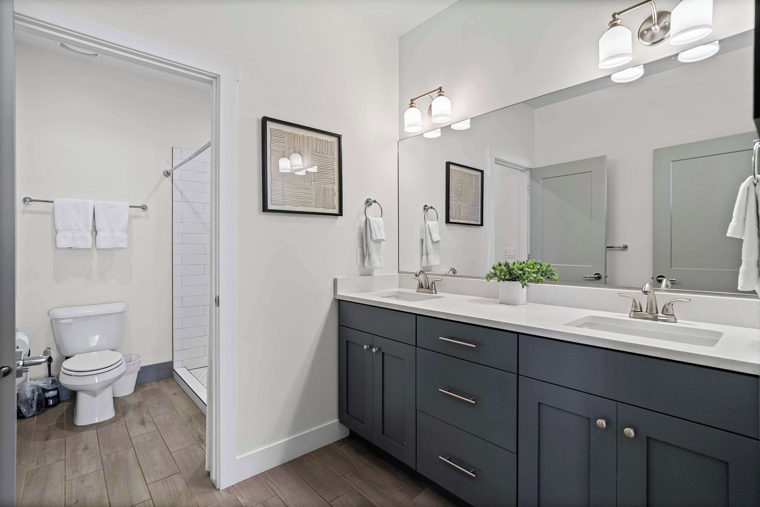 A modern bathroom with a white toilet, dark cabinets, a large mirror, and a shower area.